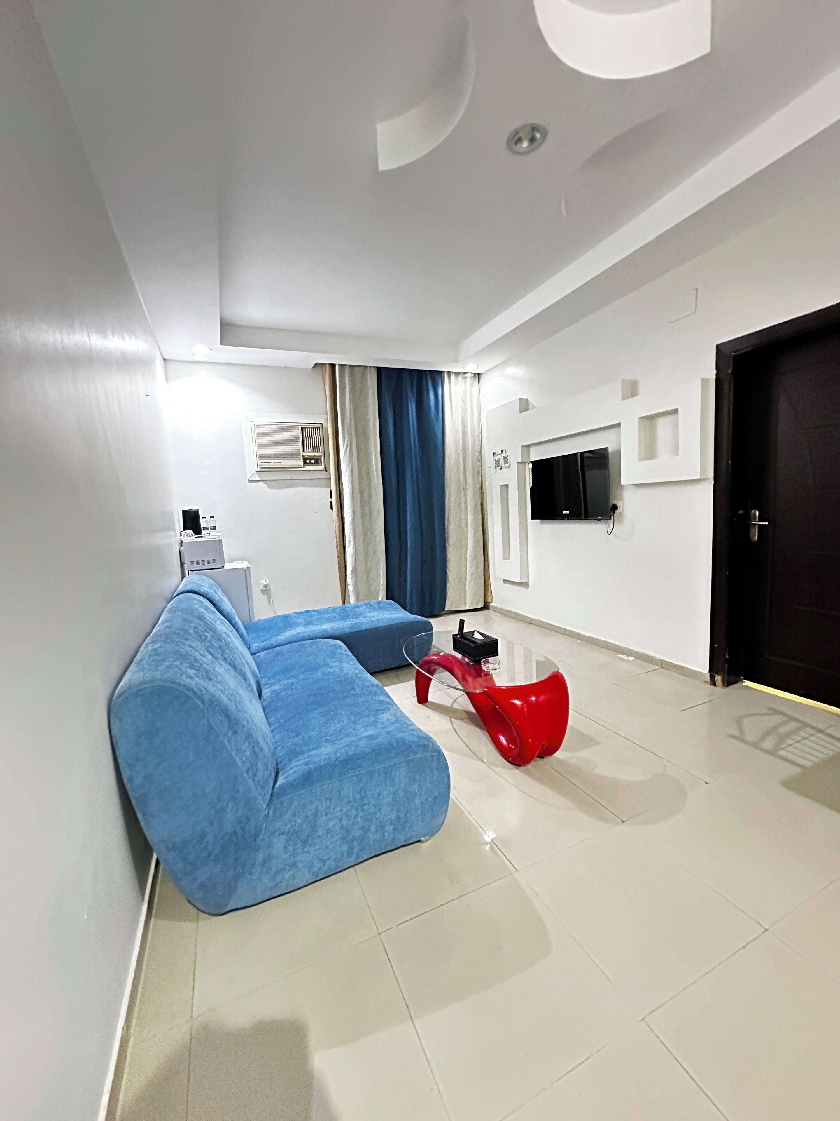 A modern living room with a sectional sofa, a red coffee table, a television, and a door.