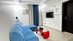 A modern living room with a sectional sofa, a red coffee table, a television, and a door.