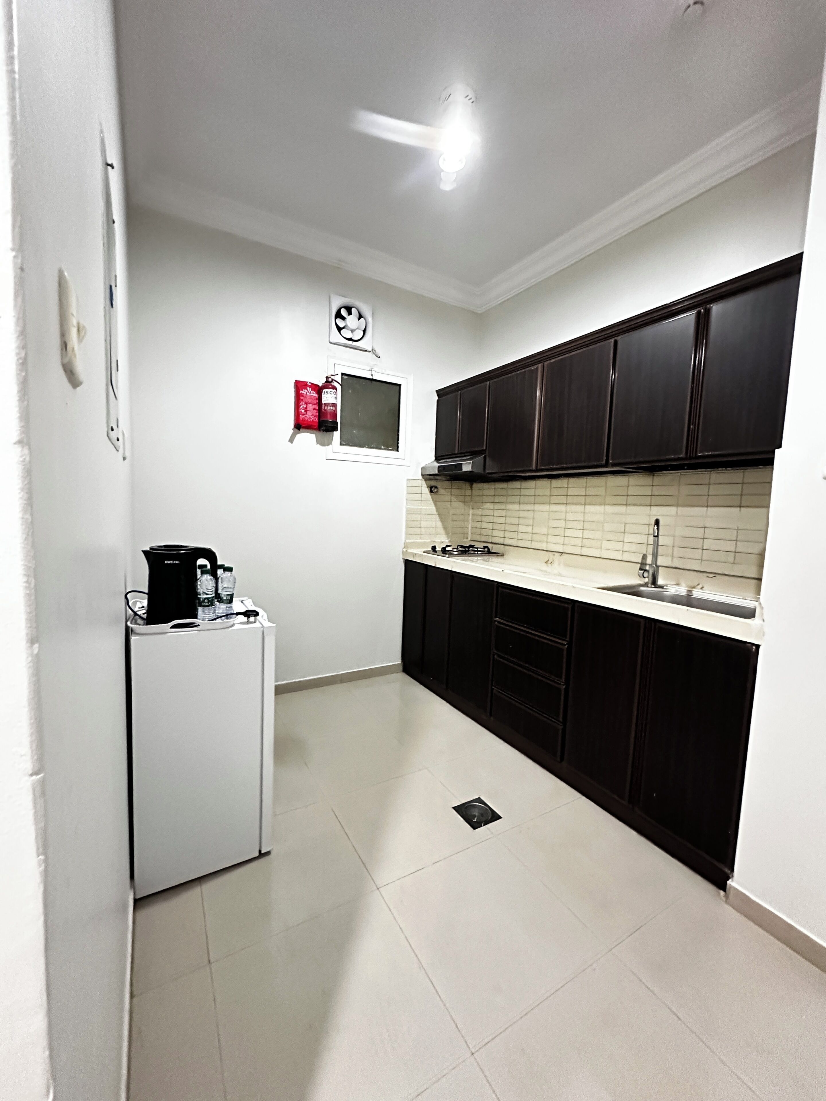 Uma cozinha compacta com geladeira, micro-ondas e armários escuros.