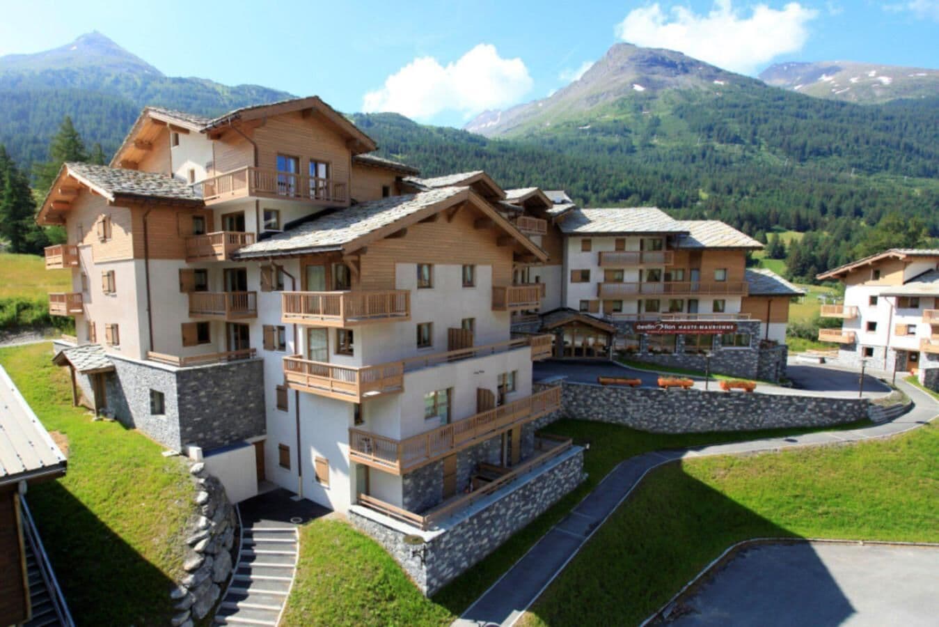 A multi-story hotel with balconies, a stone facade, and a mountainous backdrop.