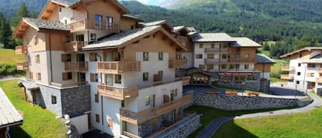 A multi-story hotel with balconies, a stone facade, and a mountainous backdrop.