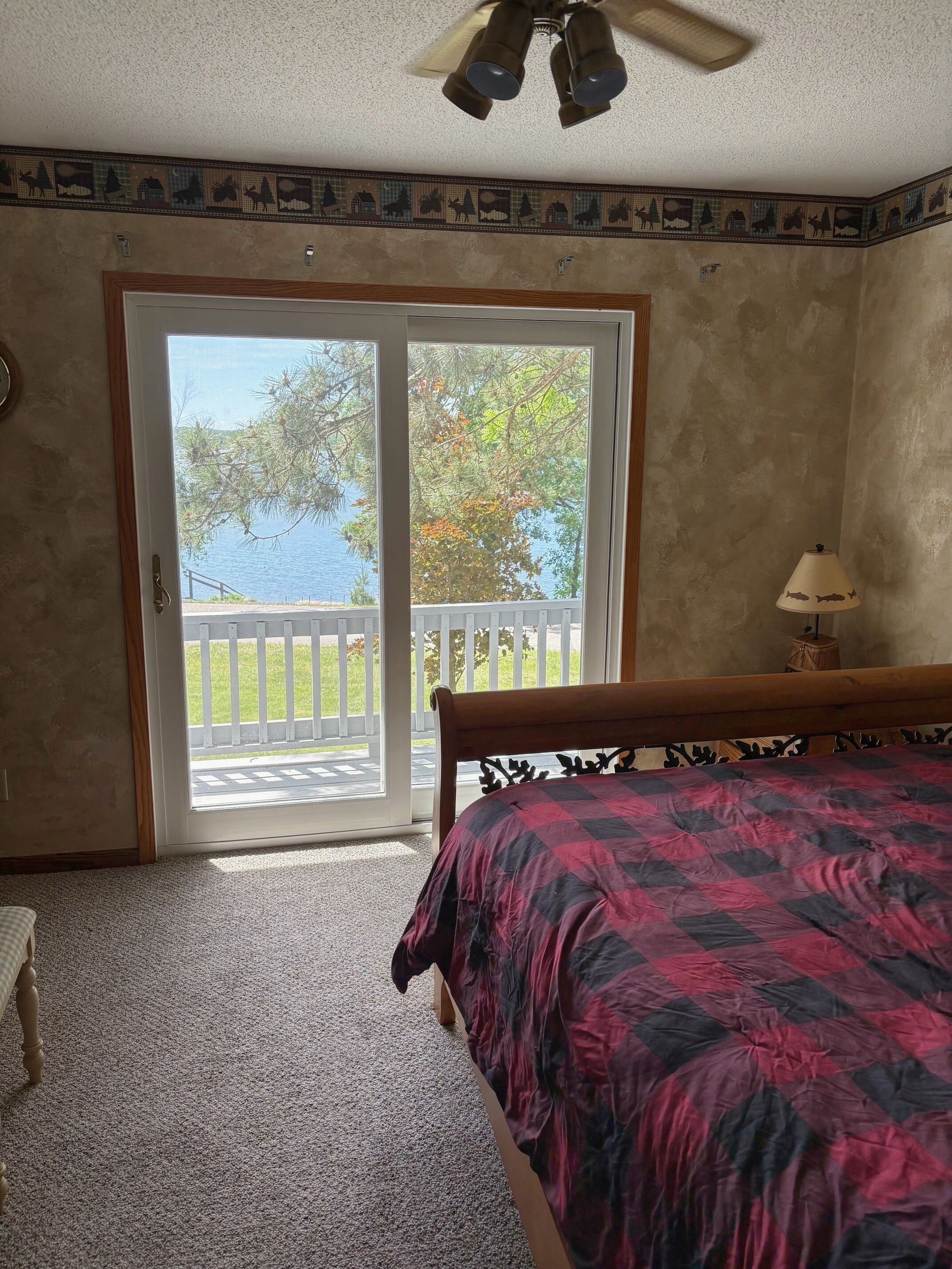 Un dormitorio con cama, ventilador de techo, lámpara y vistas a un balcón con barandilla.