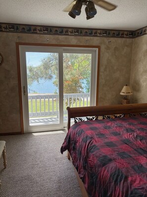 A bedroom with a bed, a ceiling fan, a lamp, and a view of a balcony with a railing.