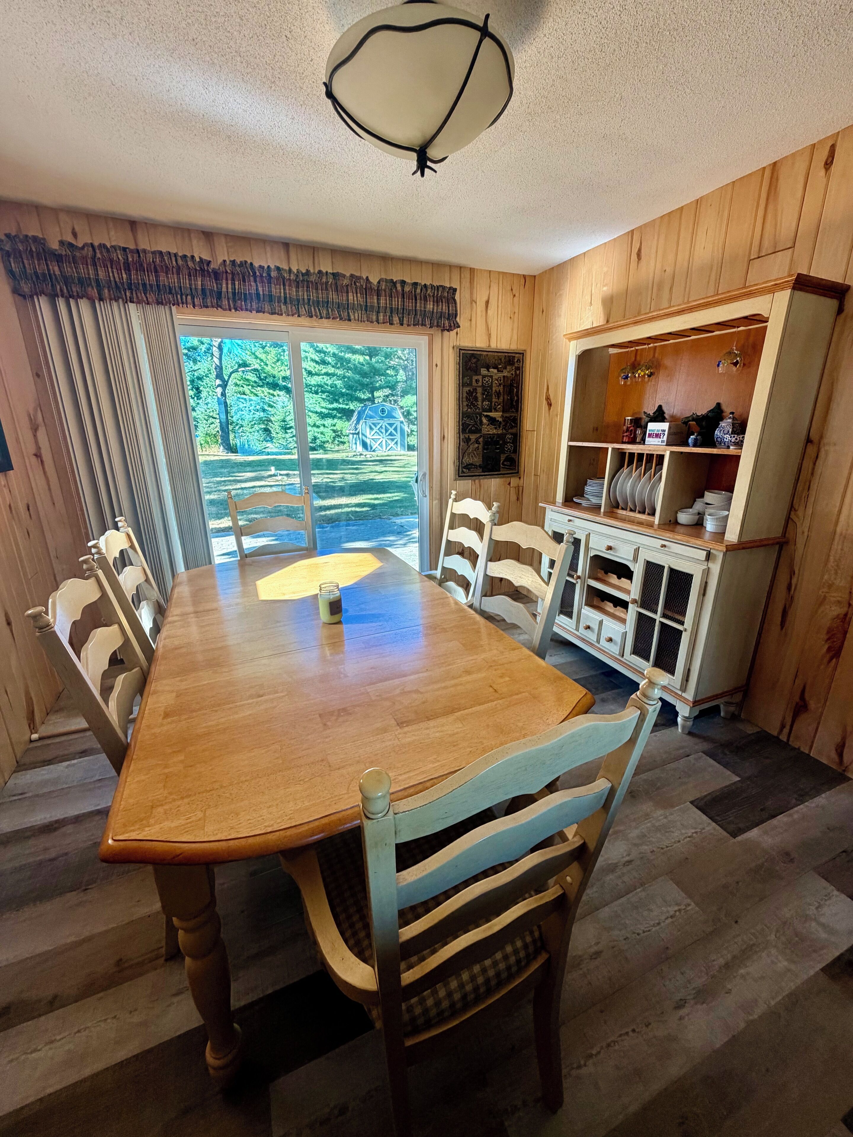 Un comedor con una mesa y sillas de madera, una ventana que da a vistas de árboles y un armario con vajilla.