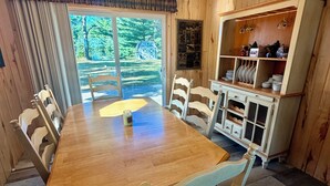 A dining area with a wooden table and chairs, a window with a view of trees, and a cabinet with dishes. - Lake Alexander Hideaway - Waterfront, Private Dock (Cushing)