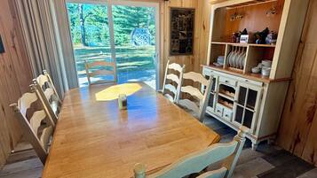 Un comedor con una mesa y sillas de madera, una ventana que da a vistas de árboles y un armario con vajilla.