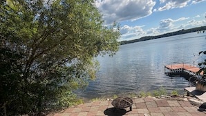 A lakeside patio with wooden chairs, a fire pit, and a dock extending into the water. - Lake Alexander Hideaway - Waterfront, Private Dock (Cushing)