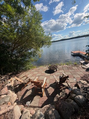 A lakeside patio with wooden chairs, a fire pit, and a dock extending into the water. - Lake Alexander Hideaway - Waterfront, Private Dock (Cushing)