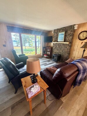 Una sala de estar con un sofá de cuero, una mesa de centro de madera, un televisor montado en una pared de piedra y una chimenea.