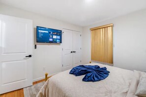 Ein Hotelzimmer mit einem Bett, einem an der Wand befestigten Fernseher und einem Fenster mit Jalousien.