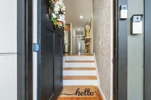 A hallway with a wooden staircase, a doormat with 'hello' written on it, and a door with a decorative wreath. - The Cozy Corner / Newark safe urban cozy stay (Newark)