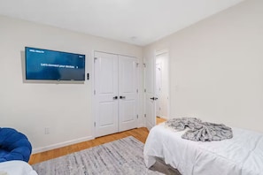 A bedroom with a television mounted on the wall, a bed with a patterned blanket, a blue bean bag chair, and a white door. - The Cozy Corner / Newark safe urban cozy stay (Newark)