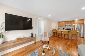 Uma sala de estar moderna com televisão de tela plana, piso de madeira e um espaço de refeições com cadeiras amarelas.