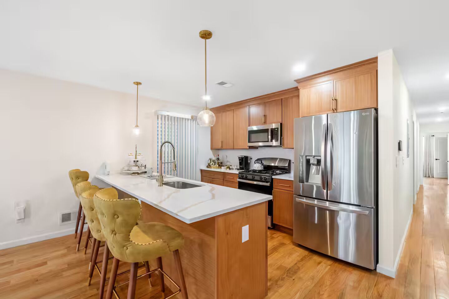 Una cocina moderna con una isla central, electrodomésticos de acero inoxidable, armarios de madera y taburetes de bar.