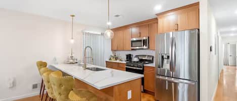 A modern kitchen with a central island, stainless steel appliances, wooden cabinets, and bar stools.