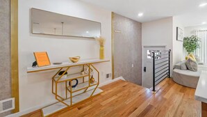 Un interior moderno con suelo de madera, una consola blanca decorada con objetos, un espejo grande y un sofá gris.