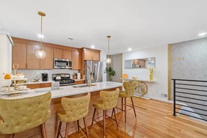 A modern kitchen with wooden cabinets, stainless steel appliances, and a central island with bar stools. - The Cozy Corner / Newark safe urban cozy stay (Newark)