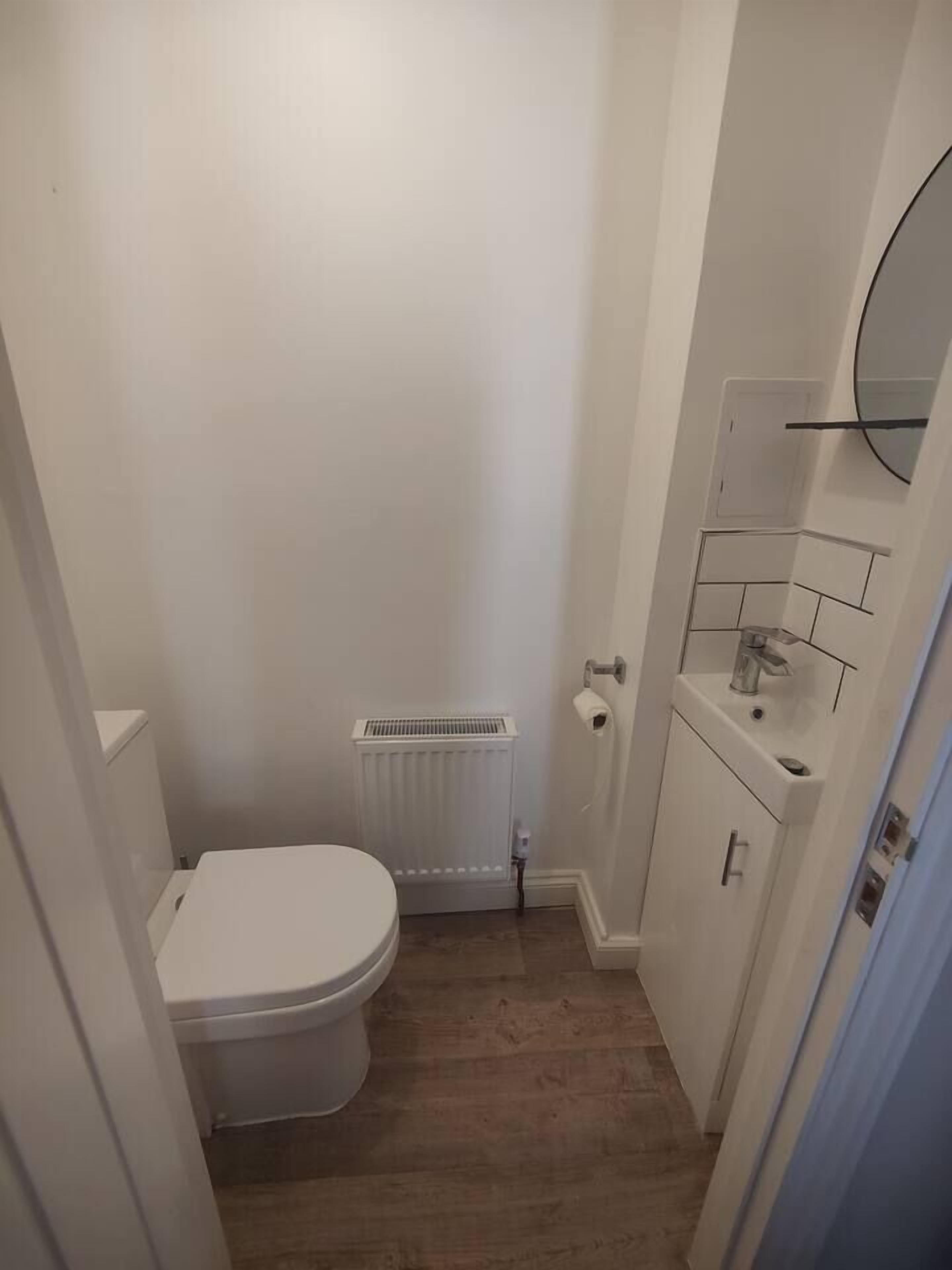 Ein kleines, schmales Badezimmer mit Toilette, Heizkörper und Waschbecken mit Spiegel darüber.