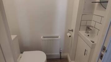 Ein kleines, schmales Badezimmer mit Toilette, Heizkörper und Waschbecken mit Spiegel darüber.
