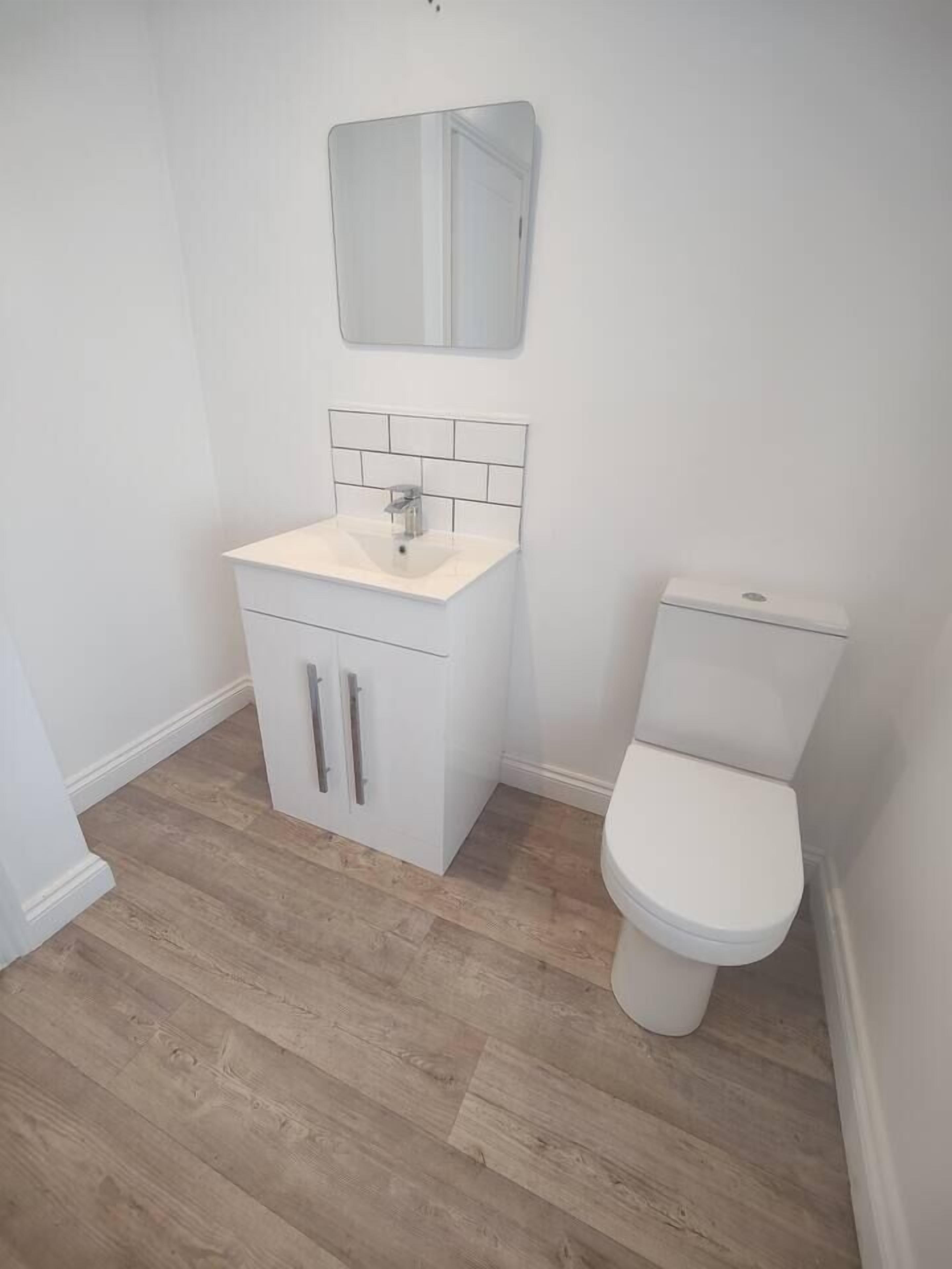 Baño con lavamanos blanco, espejo y retrete.