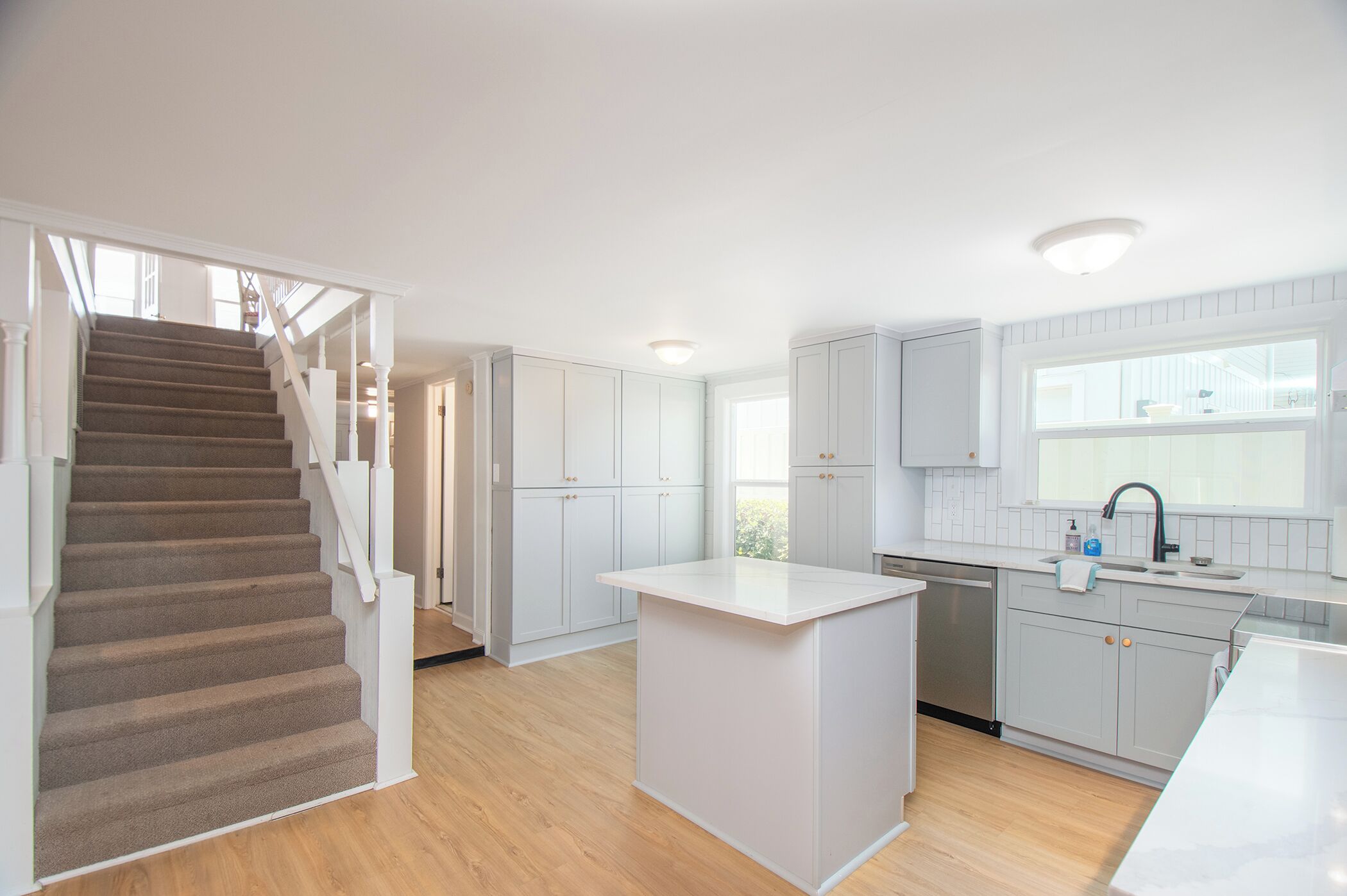 A modern kitchen with a central island, wooden flooring, and white cabinetry.