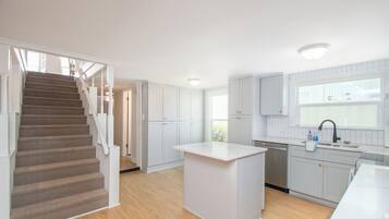 A modern kitchen with a central island, wooden flooring, and white cabinetry.