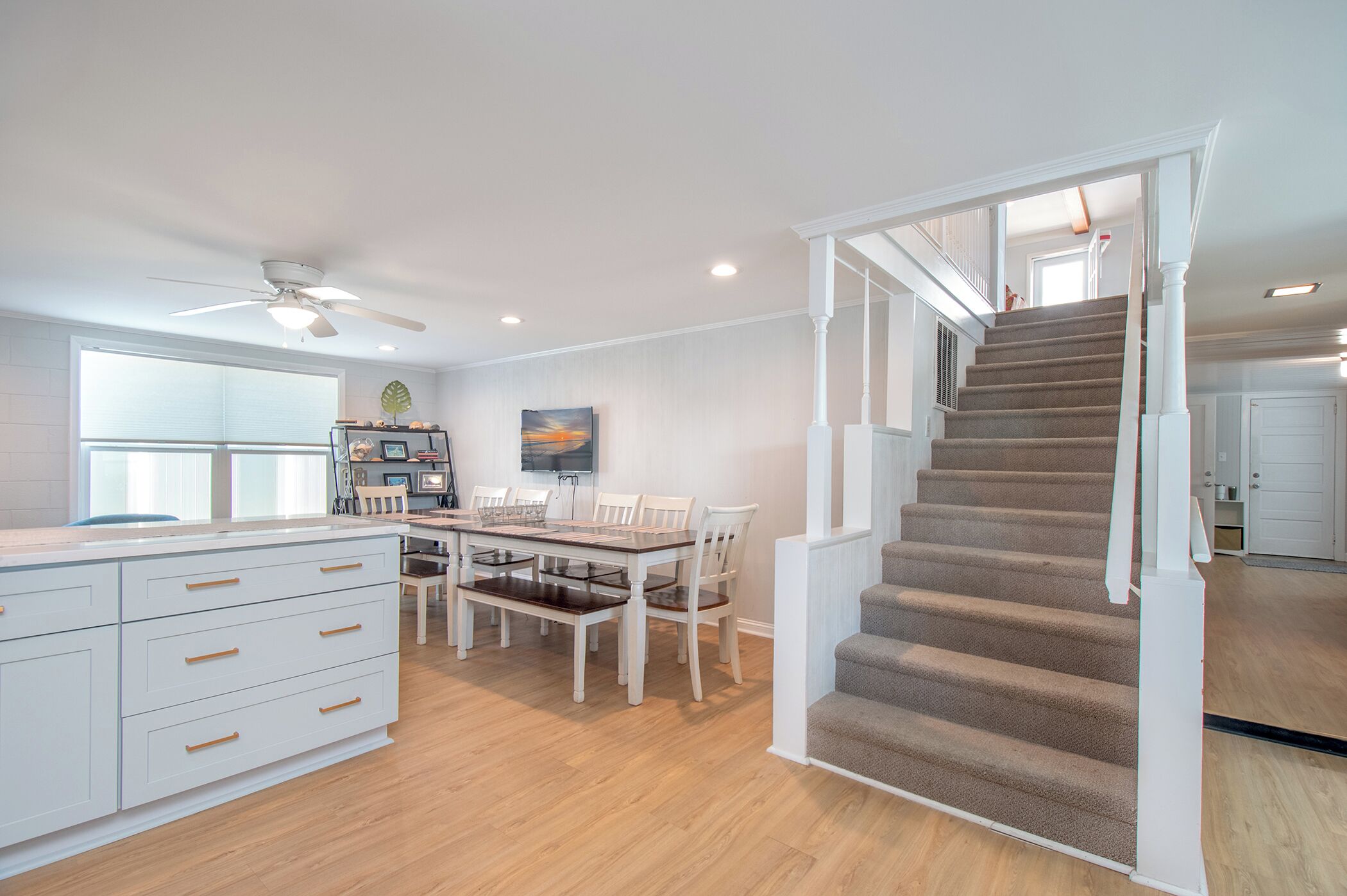 A modern kitchen with a dining area, a staircase, and a large window.