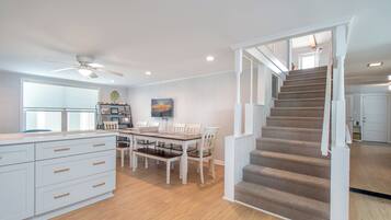 A modern kitchen with a dining area, a staircase, and a large window.