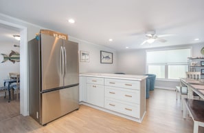 A modern kitchen with a stainless steel refrigerator, white cabinetry, and a dining area with a table and chairs. - No Pier Pressure / 3 Min Walk to Beach / Sleeps 11 (Atlantic Beach)