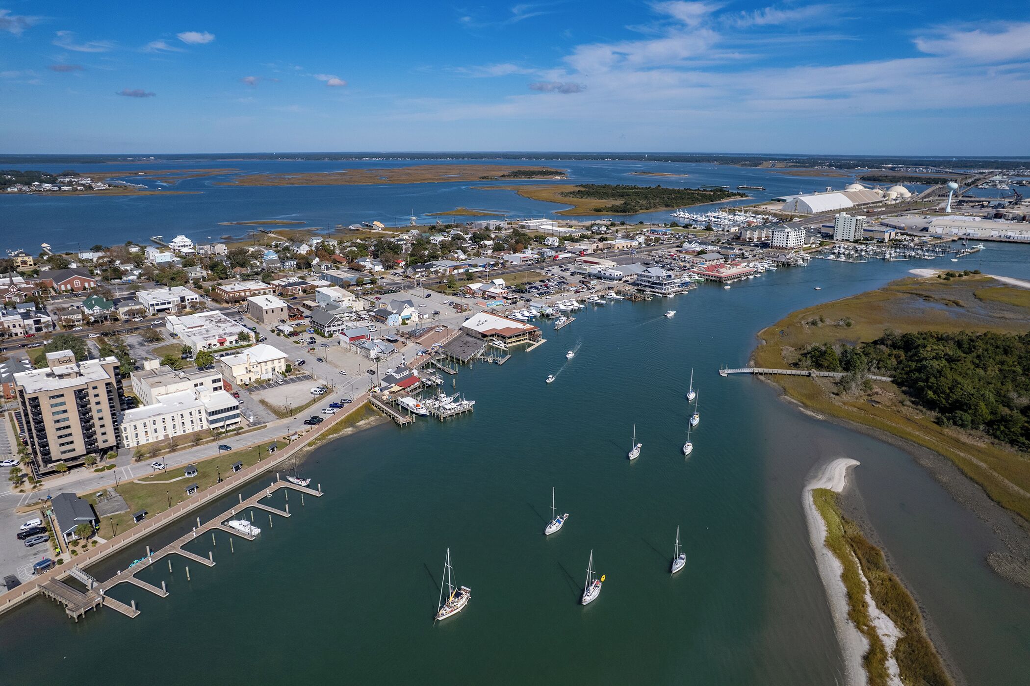 An aerial view of a coastal town with a marina, boats, and buildings.
