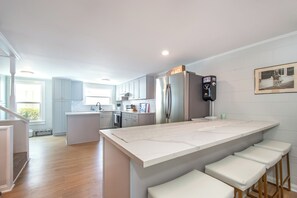 A modern kitchen with a central island, bar stools, and a refrigerator with a parking permit holder. - No Pier Pressure / 3 Min Walk to Beach / Sleeps 11 (Atlantic Beach)