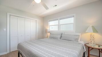 A bedroom with a bed, a ceiling fan, a window, and a bedside table with a lamp.