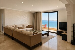 A modern living room with a sofa, a coffee table, and a television. There is a large window with a view of the sea. - Luxury Oceanfront Property with Views of Tangier Bay (Tánger)