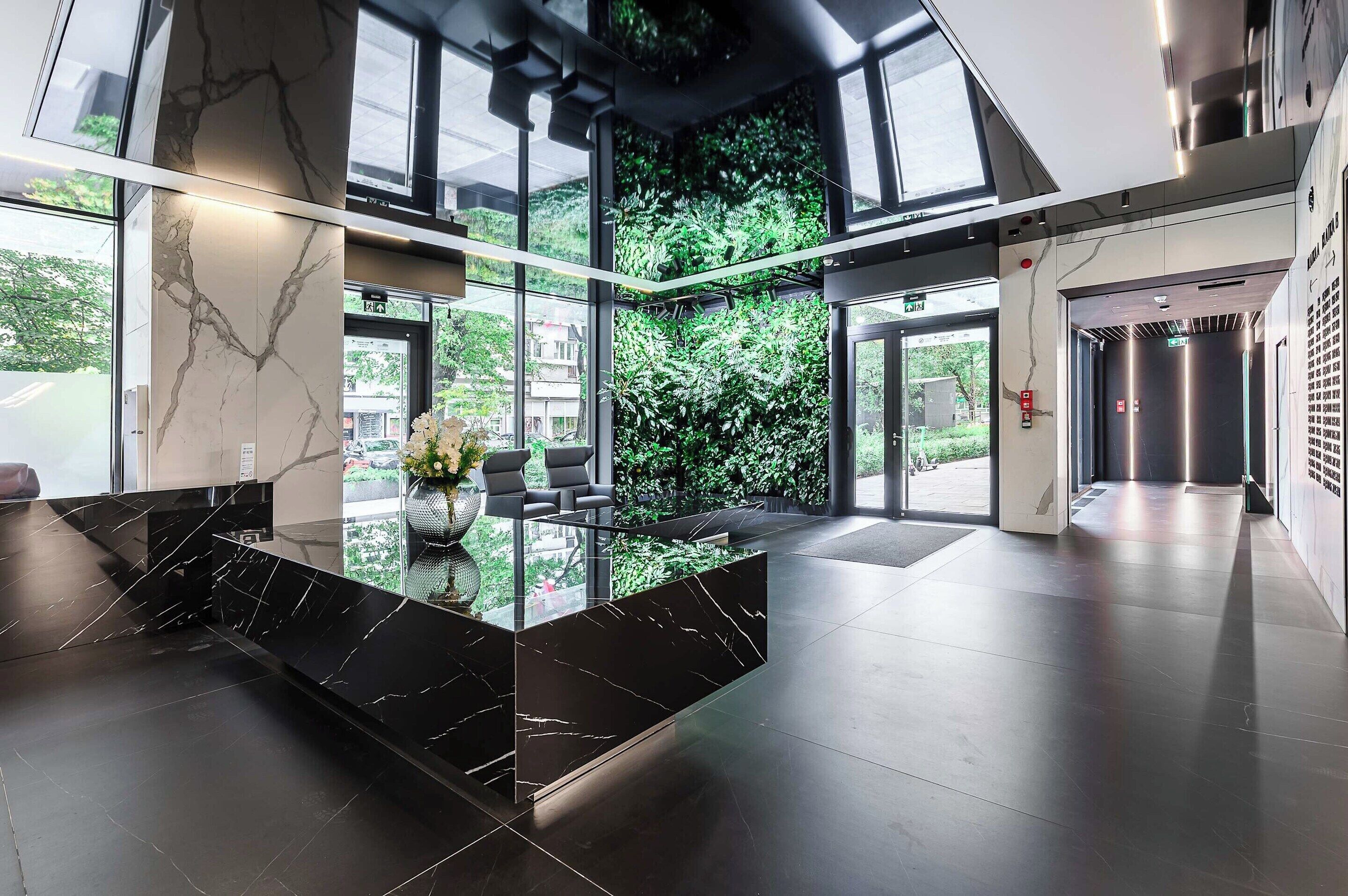 Un hall d’entrée moderne avec un comptoir de réception en marbre, un espace salon et un grand mur de verre donnant sur un paysage verdoyant.