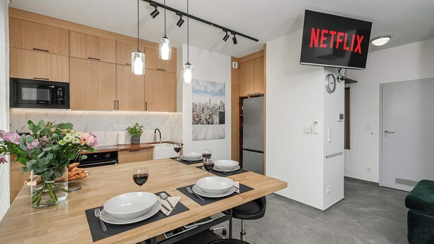 A modern kitchen with wooden cabinets, a built-in microwave, and a dining area with a table set for two. - Warsaw Flat With Balcony (Warsaw)