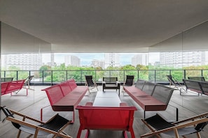 A modern lounge area with a long red sofa, multiple chairs, and a table, overlooking a cityscape. - Warsaw Flat With Balcony (Warsaw)