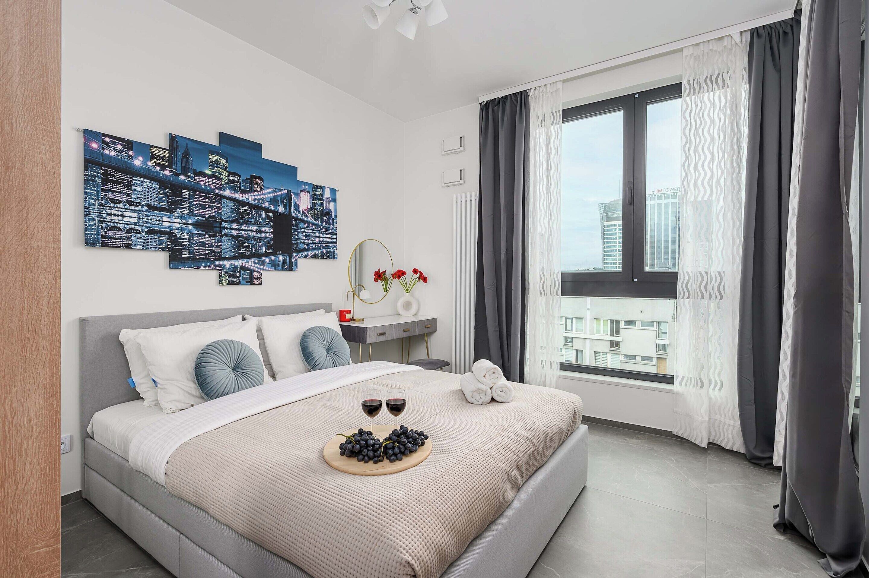 Habitación de hotel moderna con una cama grande, una obra de arte con temática urbana, vistas a edificios y una ventana con cortinas.