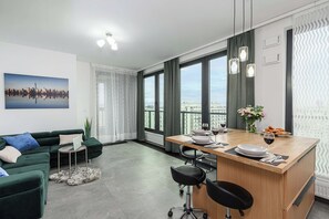 Ein modernes Wohnzimmer mit einem grünen Sofa, einem Essbereich mit einem Holztisch und großen Fenstern mit Blick auf die Stadt.
