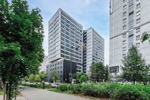 Ein modernes Hochhaus mit mehreren Stockwerken, umgeben von Grünflächen und anderen Gebäuden.