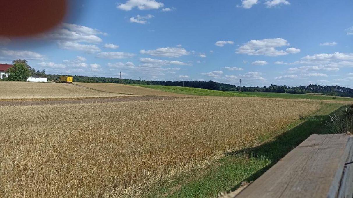Maaseutumaisema, jossa on peltoja ja kauempana näkyvä rakennus.