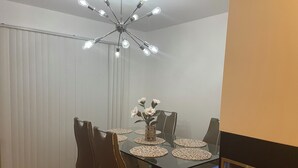 Ruokailutila, jossa on lasipöytä, mustat tuolit, maljakko kukkineen ja kattovalaisin.