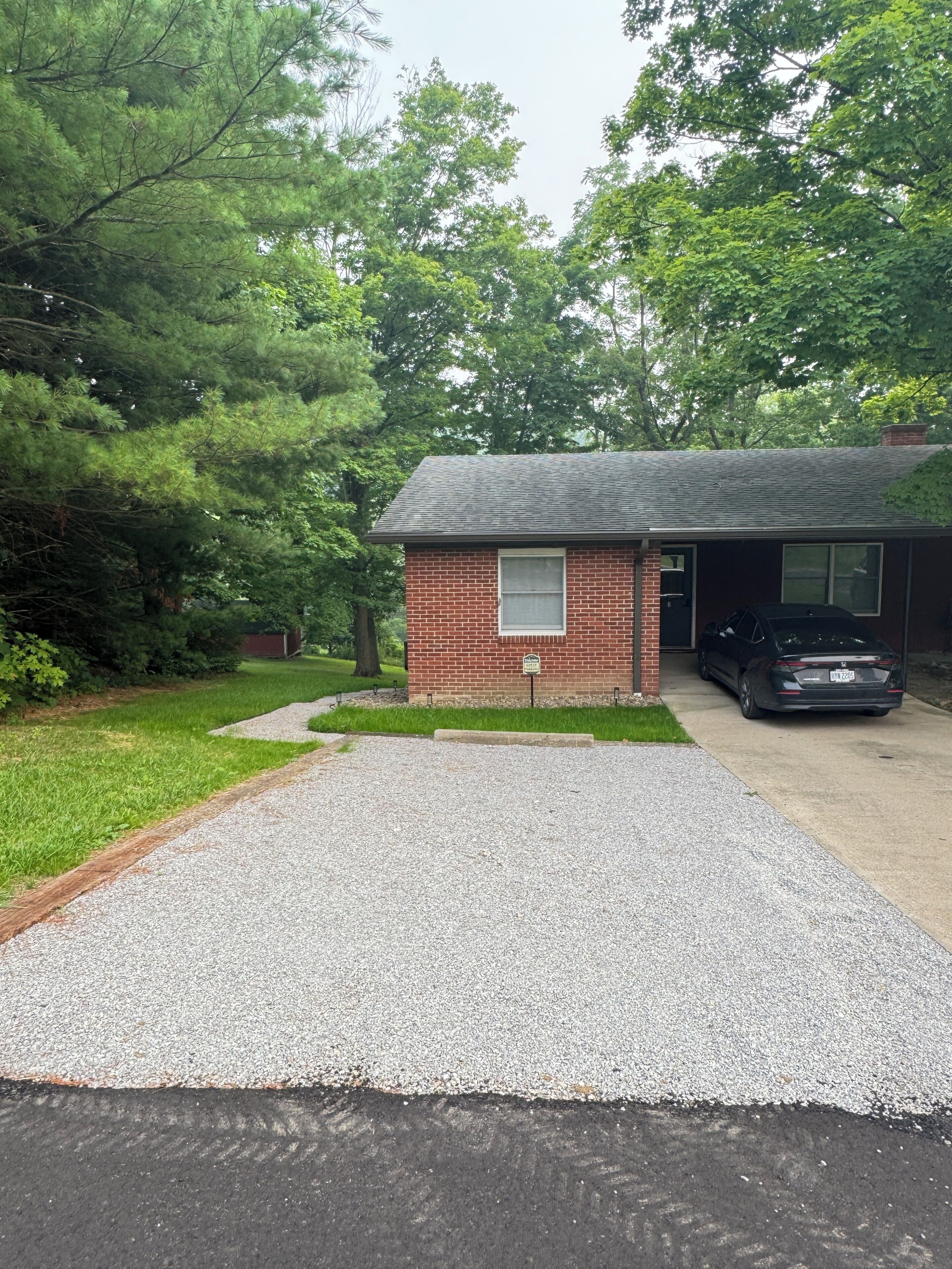 A residential property with a gravel driveway, a brick garage, and a car parked inside.