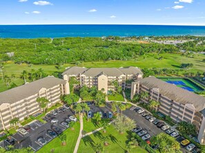 A multi-story hotel with a parking lot, surrounded by greenery and a view of the ocean. - The Divine Tides Condo 5 Min Walk to Jupiter Beach (Jupiter)