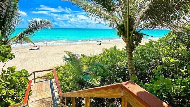 A wooden staircase leading to a beach with clear turquoise water and palm trees. - The Divine Tides Condo 5 Min Walk to Jupiter Beach (Jupiter)