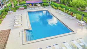 A rectangular swimming pool with lounge chairs and umbrellas, surrounded by greenery and a covered seating area. - The Divine Tides Condo 5 Min Walk to Jupiter Beach (Jupiter)