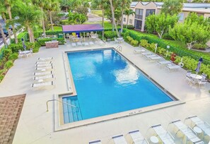 Ein rechteckiger Pool mit Liegestühlen und Sonnenschirmen, umgeben von viel Grün und einem überdachten Sitzbereich.