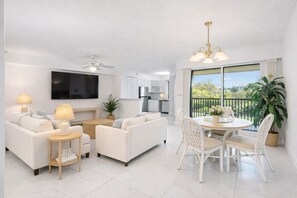 A modern living room with a flat-screen TV, white sofas, a dining table with chairs, a ceiling fan, and a view of the outdoors. - The Divine Tides Condo 5 Min Walk to Jupiter Beach (Jupiter)