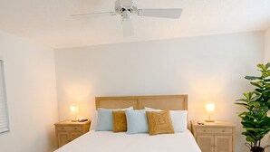 A bedroom with a large bed, two bedside tables with lamps, a ceiling fan, and a potted plant. - The Divine Tides Condo 5 Min Walk to Jupiter Beach (Jupiter)