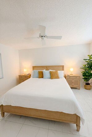 Ein Schlafzimmer mit einem großen Bett, zwei Nachttischen mit Lampen, einem Deckenventilator und einer Topfpflanze.