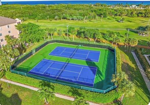 Un court de tennis entouré de verdure et un immeuble d’habitation.